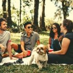 A group of students sitting on a white picnic blanket with a dog in front of them.