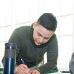 A male student is writing on a paper on the desk.