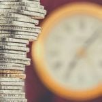 A stack of coins with a clock in the background.