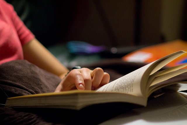 An open book with a hand pointing on it.
