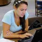 Female college student scrolling through her laptop and studying in the library.