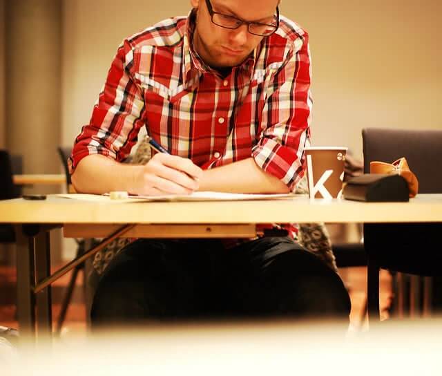 A male student wearing red checkered polo, writing on the desk.