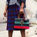 A model wearing a plaid skirt and holding a striped bag.