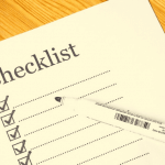 A piece of paper that says "checklist" with lines underneath and a pen sitting on top.
