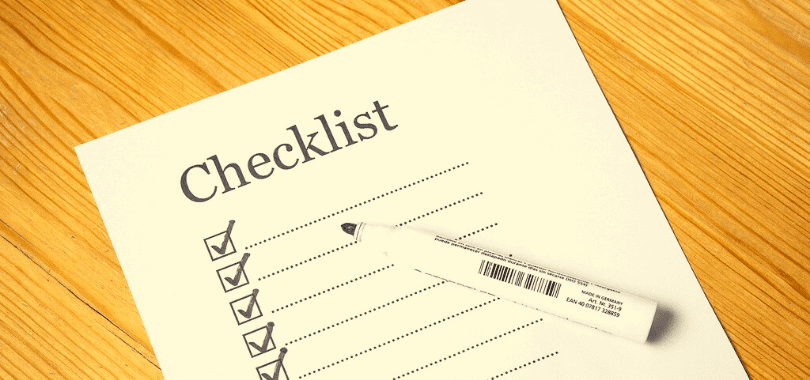 A piece of paper that says "checklist" with lines underneath and a pen sitting on top.
