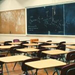 An empty high school classroom with beige desks and brown chairs.