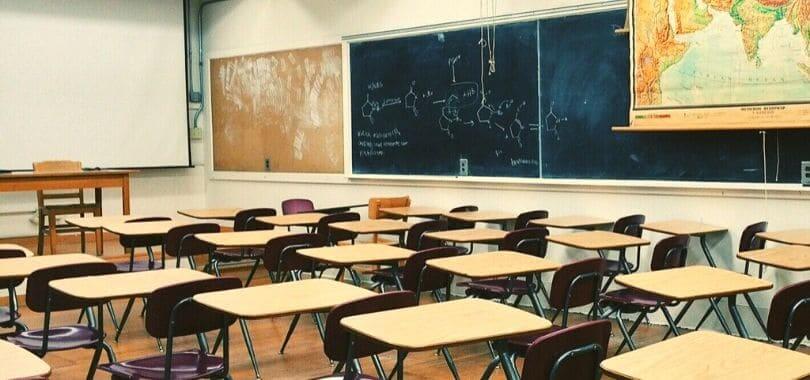An empty high school classroom with beige desks and brown chairs.