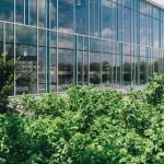 A glass building surrounded by green bushes.