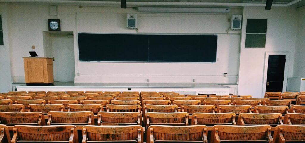 A lecture hall with brown chairs and a blackboard in front.