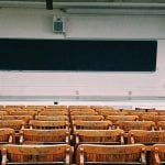 A lecture hall with brown chairs and a blackboard in front.