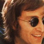 John Lennon is smiling and wearing shades.