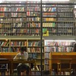 Man studying alone on his Macbook at the library showing bunch of books behind him.