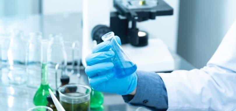 A scientist holding a flask filled with a blue liquid.