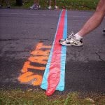 A foot stepping on the track line with the word "Start" painted on the ground.