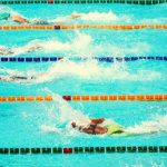 Four student swimmers competing in multiple pool lanes.