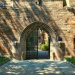 A metal gate with one door open on a college campus.