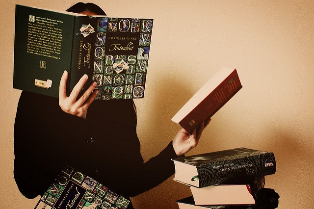 A girl covering her face with an open book while holding another book on the left hand.