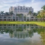 Florida International University building surrounded with coconut trees and a lake in the foreground.