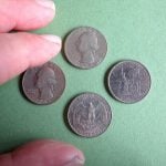 Three fingers almost touching four old US coins against a green background.