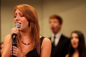 A girl singing and two backup singers blurred in the background.