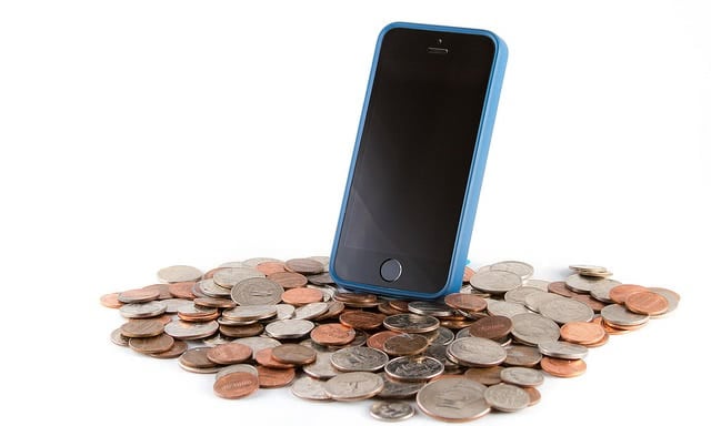 A smartphone is standing on a pile of coins.