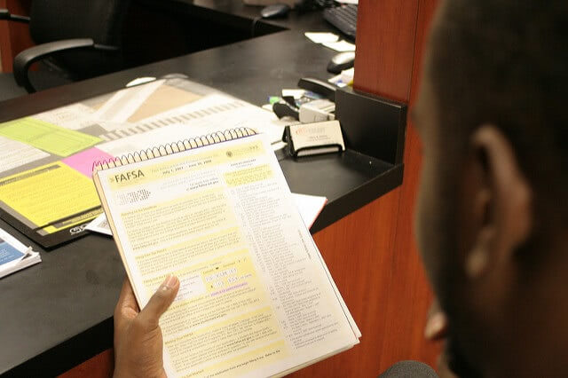 A man is holding a FAFSA form - showing a half side of his head on the foreground.
