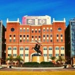 A college arena with a statue of a man on a horse in front of it.