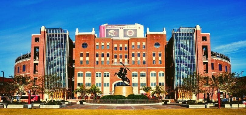 A college arena with a statue of a man on a horse in front of it.