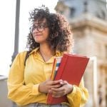 A student in a yellow jacket holding a red binder.