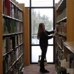 A woman standing between two shelves looking for a book.