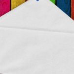 A white envelope pinned against a rainbow wooden board.