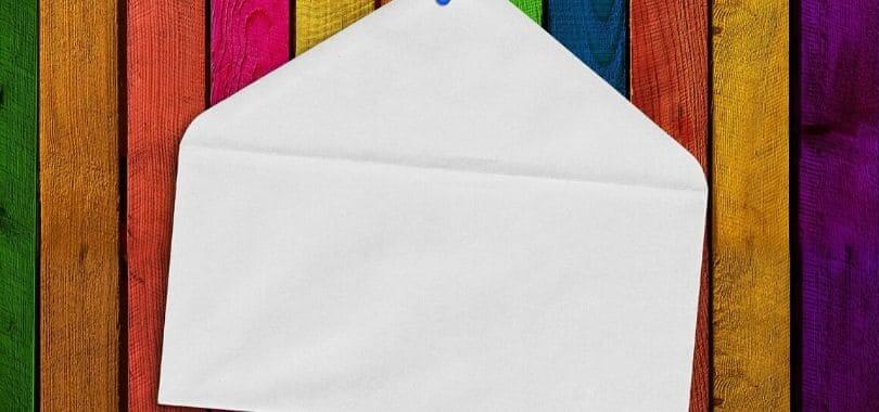 A white envelope pinned against a rainbow wooden board.