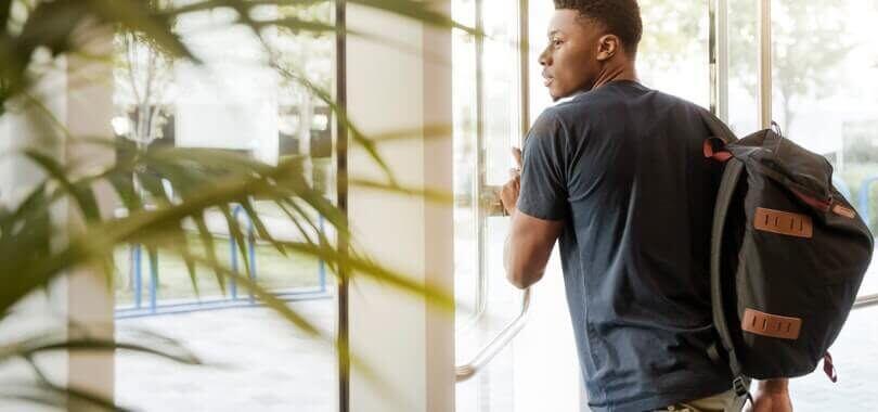 Student pushing open a door, with a plant in the foreground.
