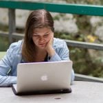 A woman is looking at her laptop with her hand is holding her face.