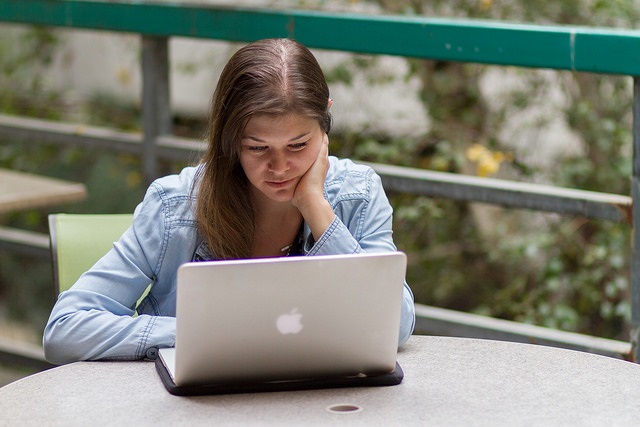 A woman is looking at her laptop with her hand is holding her face.