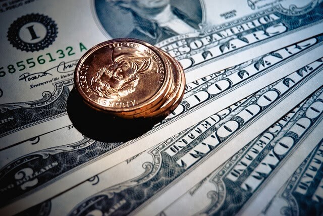 Pile of three bronze coins over a pile of dollar bills.