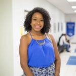 Image of a smiling black woman standing in the hallway.