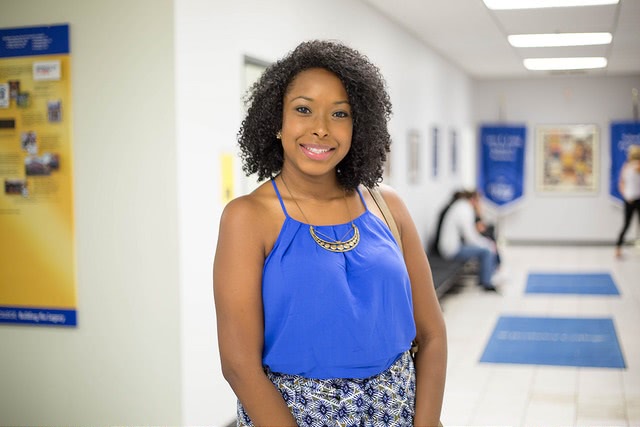 Image of a smiling black woman standing in the hallway.