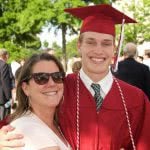 A portrait of a young man wearing a red graduation gown with his mom on his side.