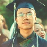 A college student wearing graduation robes looking forward.