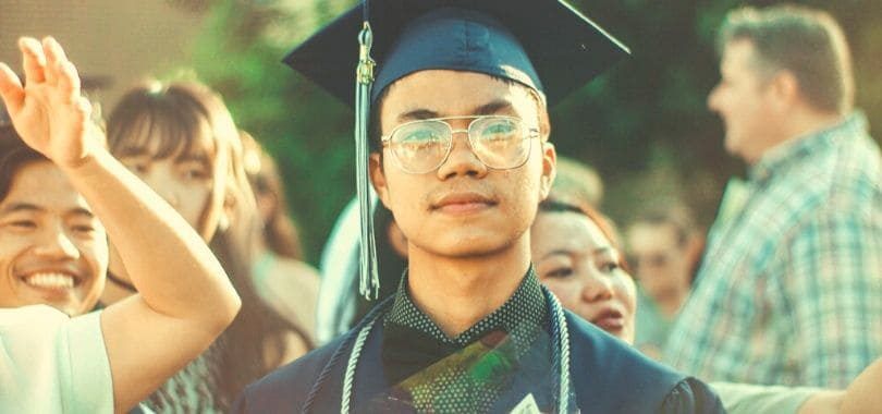A college student wearing graduation robes looking forward.