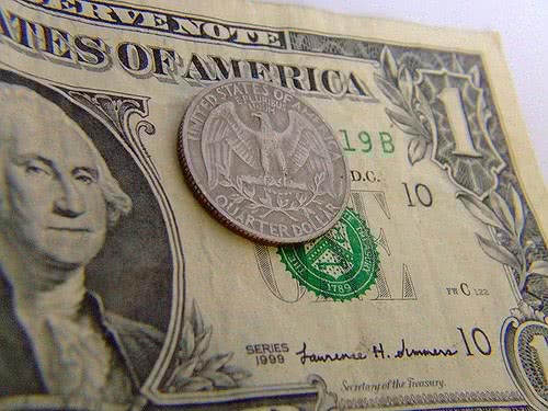 Quarter dollar coin placed over a one dollar bill.