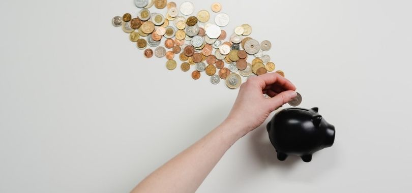 Various coins coming out of a black piggy bank.
