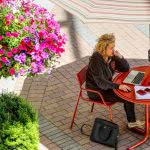 Aerial view of a woman using her laptop on a steel table with an umbrella on a bright sunny day.