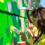 A girl is painting on the wall.