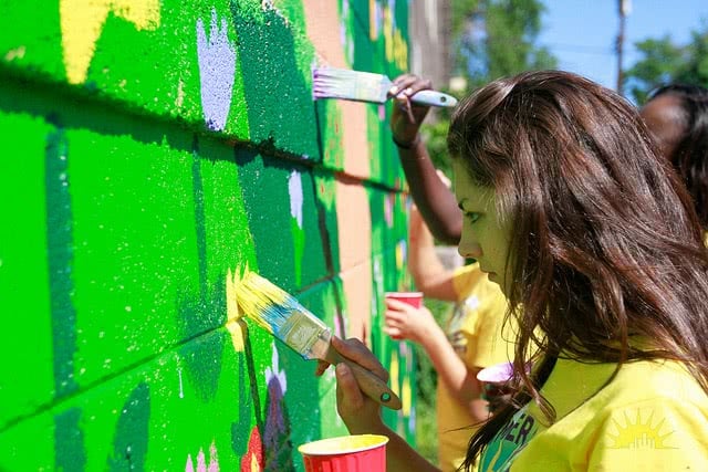 A girl is painting on the wall.