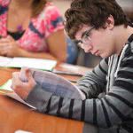 A male student is reading something on a white paper.