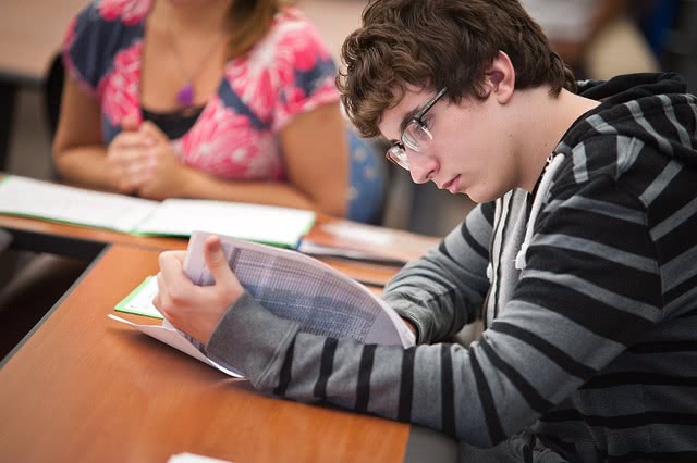 A male student is reading something on a white paper.