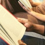 Students holding open textbooks against their legs.