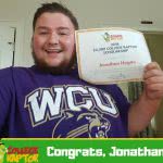 A young male student smiling while holding a $2500 College Raptor Scholarship certificate near his face.